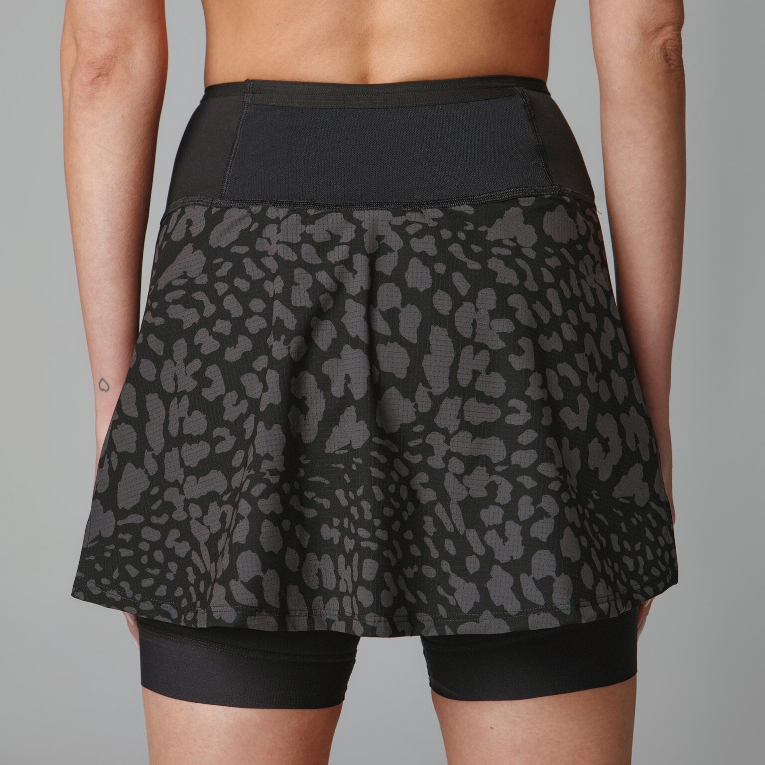 A model in a black and gray running skirt with built-in shorts and back pockets. All made of high-performance fabrics.