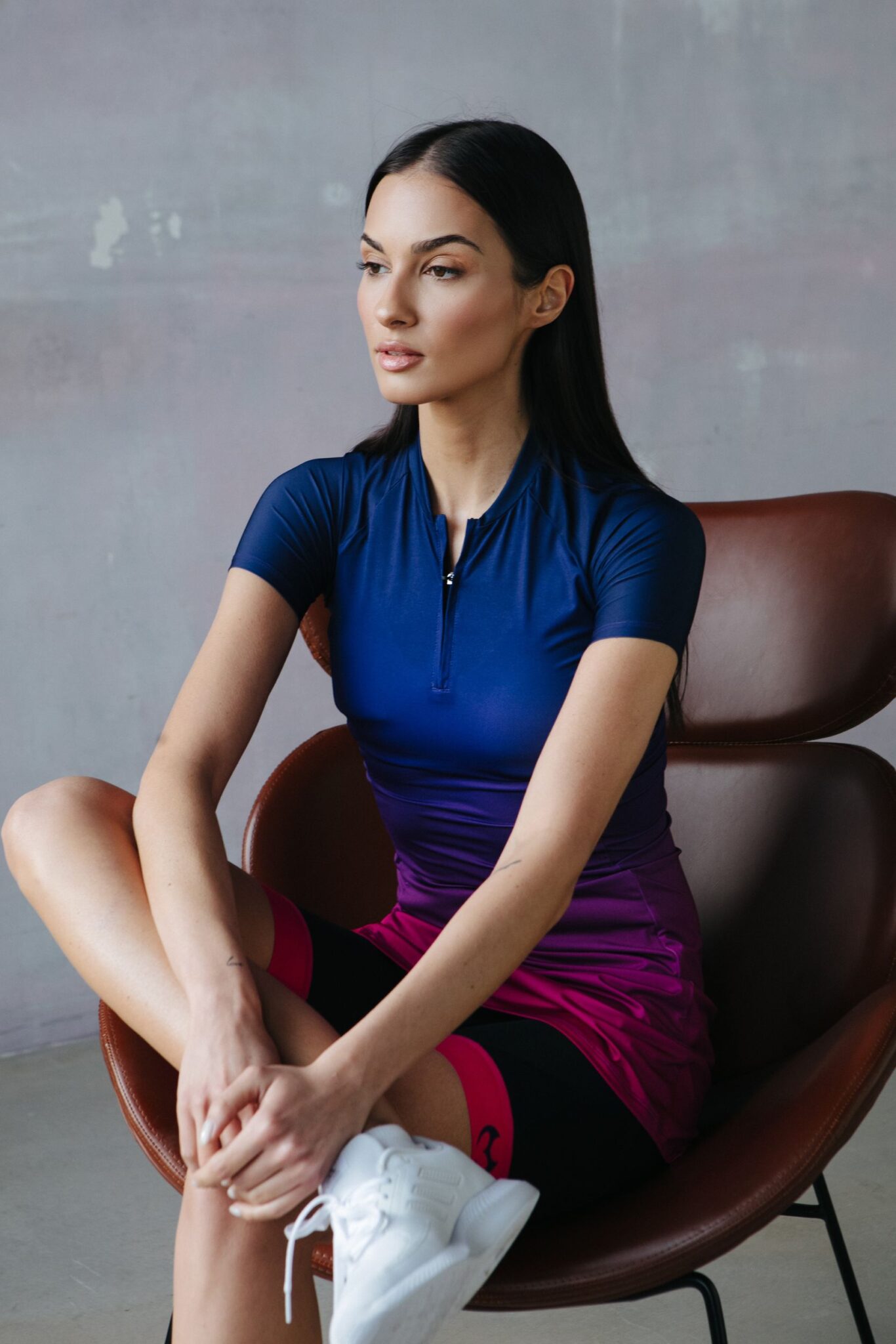A model in a navy blue and purple sports dress with shorts is sitting on a chair.